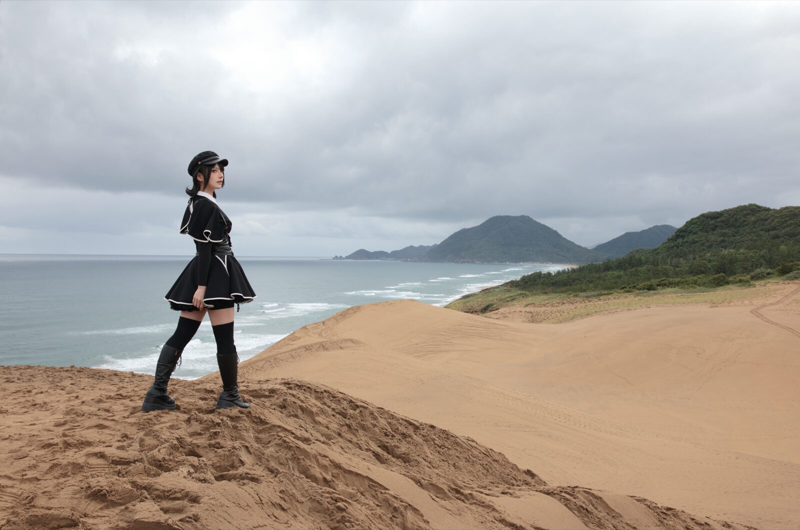 曇天の砂丘の稜線に立ち、海を見る人物