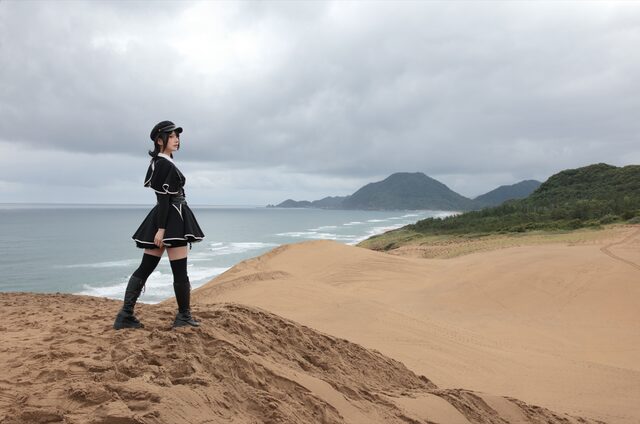 曇天の砂丘の稜線に立ち、海を見る人物